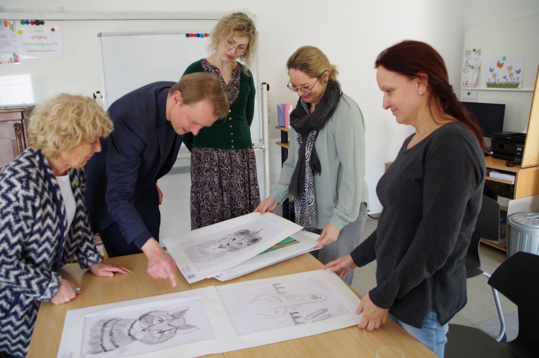 Lore Hauschild (Fraktionsvorsitzende Bündnis 90/Die Grünen, Greven), Jan-Niclas Gesenhues (Bundestagsabgeordneter Bündnis 90/Die Grünen), Rita Zimmermann (Sprecherin Bündnis 90/Die Grünen, Greven), Svetlana Kriger und Ludmila Schlegel (Modellierton e.V.) schauen sich Zeichnungen auf einem Tisch an.