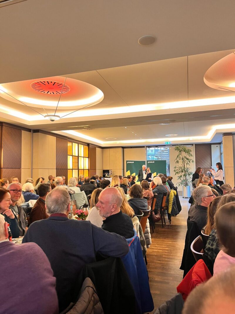 In einem großen Saal sitzen viele Mitglieder und hören einem Vortrag zu